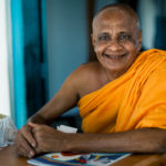 Portrait of elderly Asian buddhist monk smiling at camera in buddhist monastery at river in Madu Ganga, Sri Lanka.